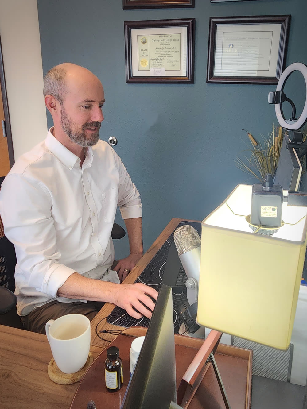 Dr. Andrew Rostenberg recording in his podcast studio — ring light, professional microphone, chiropractic credentials on wall