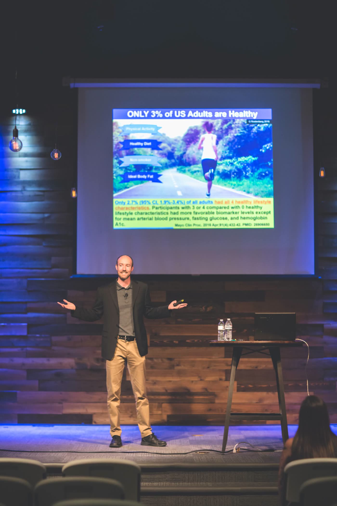 Dr. Andrew Rostenberg speaking on stage — arms wide, full audience engagement
