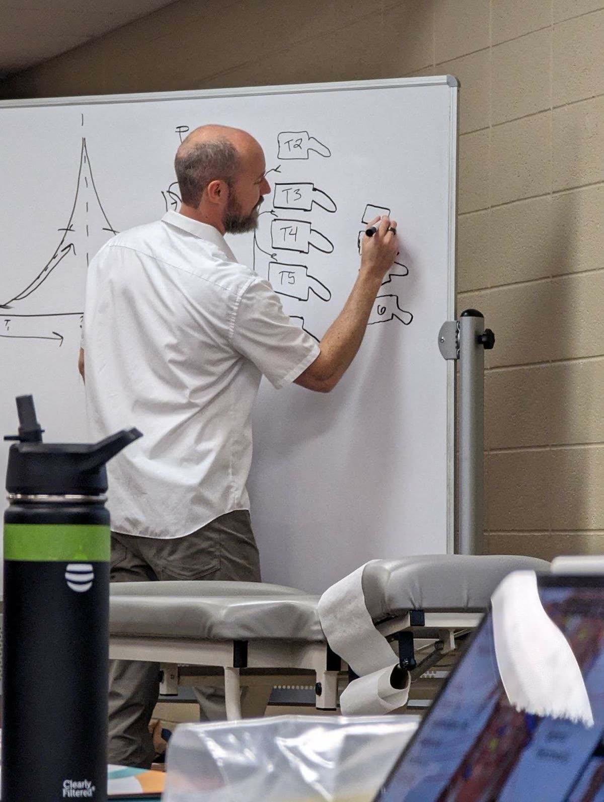 Dr. Rostenberg drawing spinal anatomy on a whiteboard — T2 through T6 vertebrae — during a clinical seminar